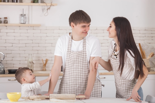 Adorável família cozinhar togrther. Família jovem na cozinha tomando café da manhã ou jantar. Mãe, pai e seu filho pequeno preparando a refeição.