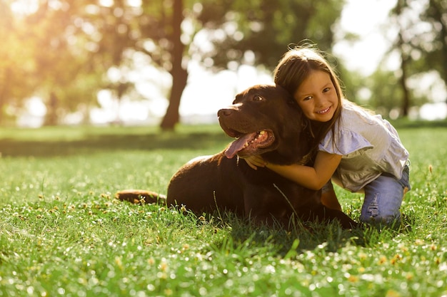 Adorável garota abraçando cachorro e olhando para a câmera no parque