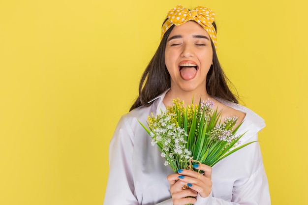 Adorável garota fecha os olhos e tira a língua no fundo amarelo com um monte de flores foto de alta qualidade