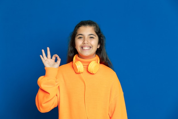 Adorável garota pré-adolescente com camisa amarela, gesticulando sobre parede azul