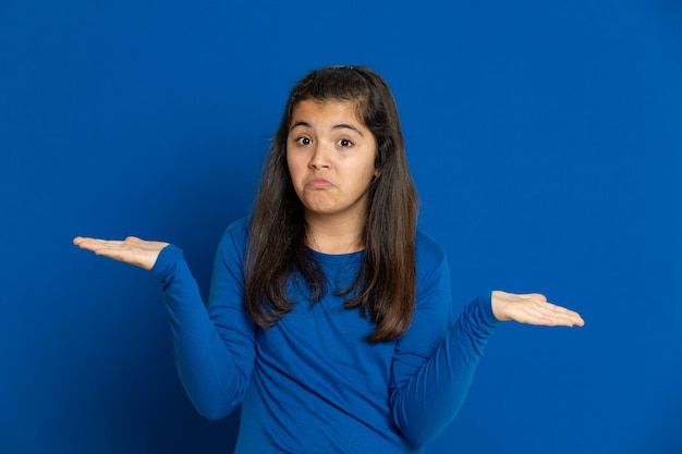 Adorável garota pré-adolescente com camisa azul, gesticulando sobre parede azul