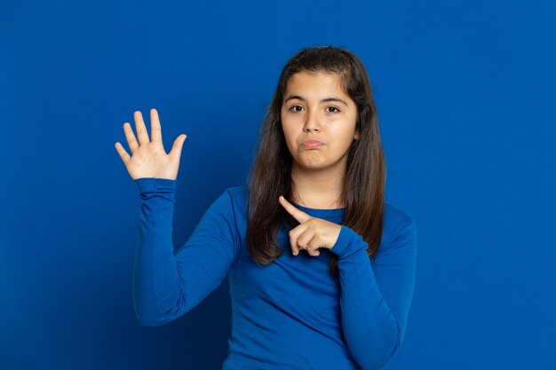 Adorável garota pré-adolescente com camisa azul, gesticulando sobre parede azul