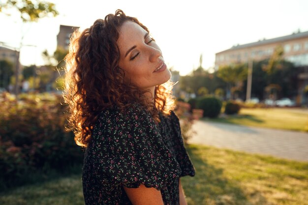 Adorável garota ruiva cacheada com sardas em um vestido gosta de bom tempo sentada no gramado