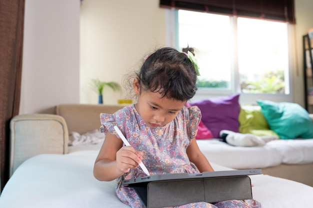 Adorável garota sentada no sofá usando tablet em casa conceito de aprendizagem em casa