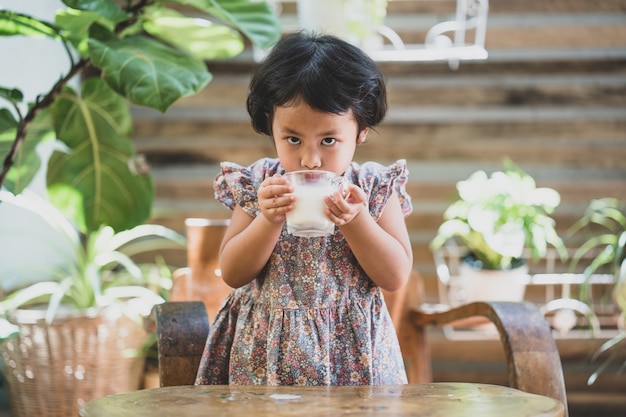 Adorável garota tomando leite em uma mesa de madeira