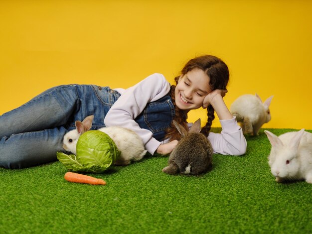 Adorável garotinha está deitada brincando com os coelhinhos no estúdio amarelo