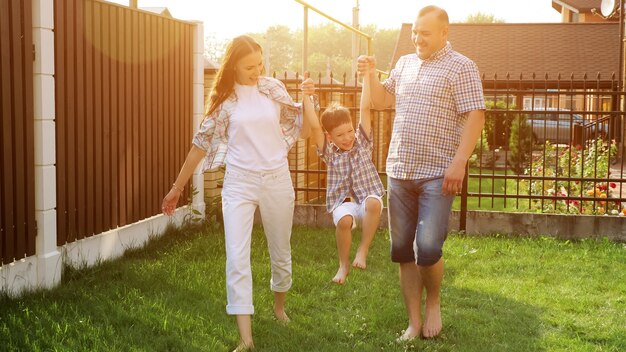 Foto adorável garotinho de short branco segurando as mãos da mãe e do pai, andando e pulando