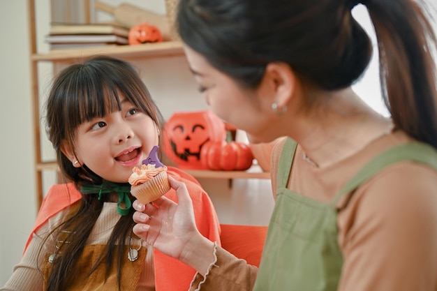 Adorável jovem asiática em uma fantasia de Halloween está comendo um cupcake com sua mãe