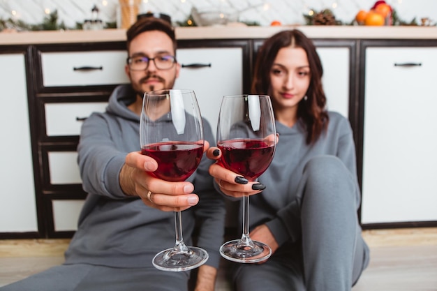 Adorável jovem casal sentado cozinha bebendo vinho em copos, guirlandas para casa aconchegante interior