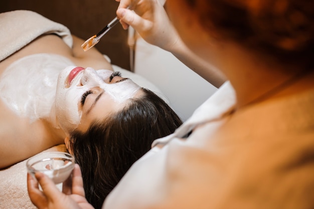 Foto adorável jovem fêmea relaxando ao fazer procedimentos faciais em um salão de spa de bem-estar.