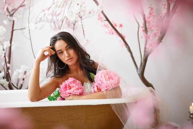 Adorável jovem modelo sentado em uma banheira com um monte de flores Foto de alta qualidade