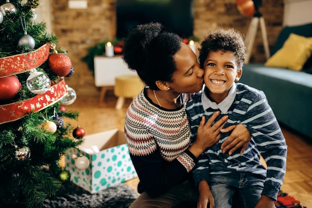 Adorável mãe afro-americana beijando seu filho feliz no Natal