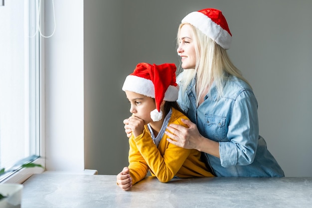 Adorável mãe loira caucasiana com filha usando bonés de papai noel