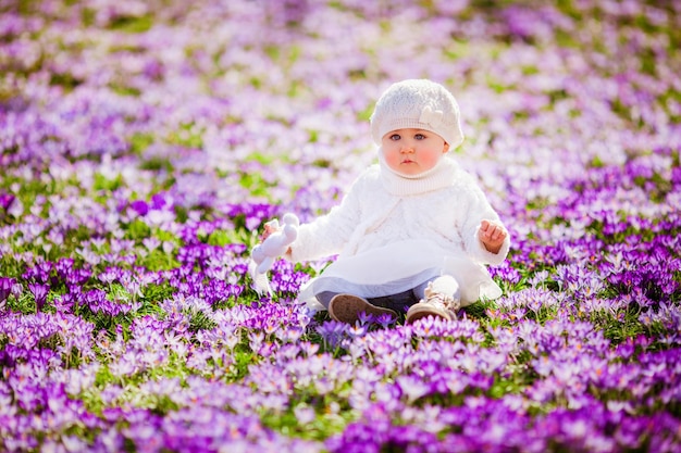Foto adorável menina aproveitando a primavera e o sol entre os açafrões de flores da primavera