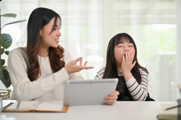 Adorável menina asiática bocejando enquanto sua mãe está ensinando matemática no tablet em casa