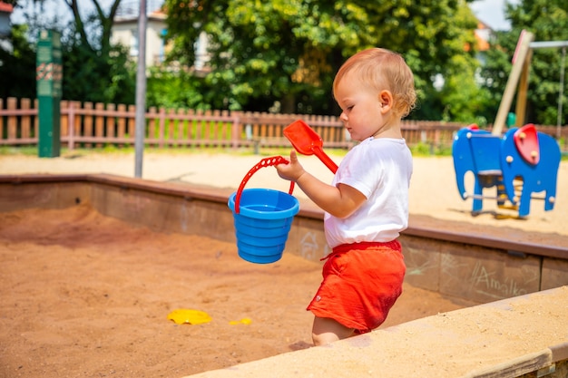 Adorável menina brincando com areia na caixa de areia no parquinho