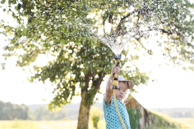 Adorável menina brincando com uma mangueira de jardim em dia quente e ensolarado de verão