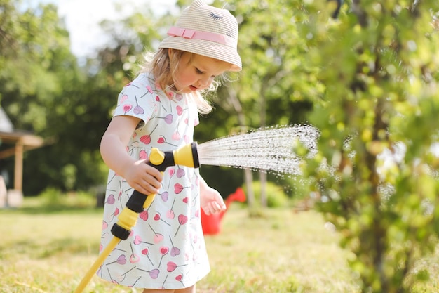 Adorável menina brincando com uma mangueira de jardim em dia quente e ensolarado de verão