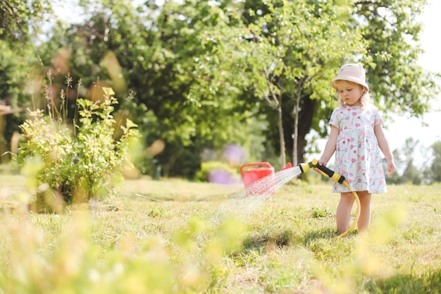 Adorável menina brincando com uma mangueira de jardim em dia quente e ensolarado de verão