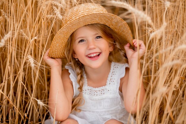 Adorável menina brincando em um campo de trigo em um dia quente de verão