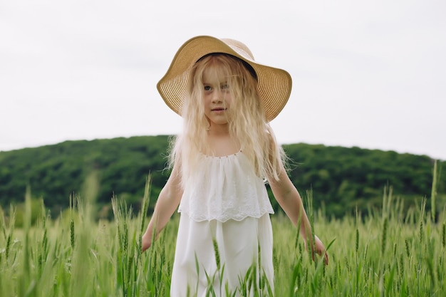 Adorável menina brincando no campo de trigo em um dia quente de verão