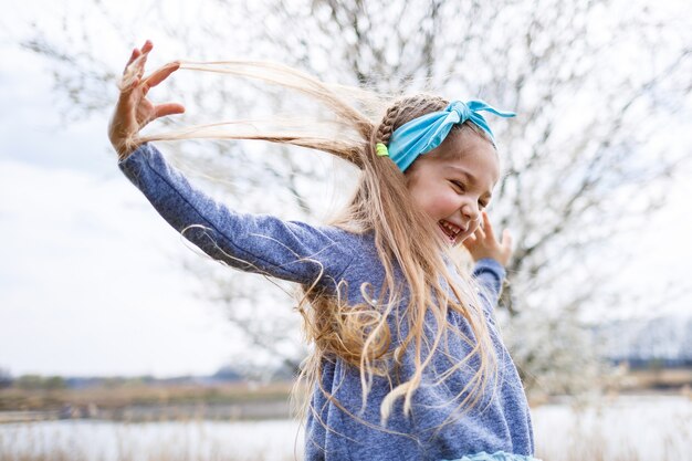 Adorável menina brincando no jardim de macieira florescendo na caça aos ovos de páscoa, correndo e sorrindo. criança no pomar de frutas da primavera com flor de cerejeira.