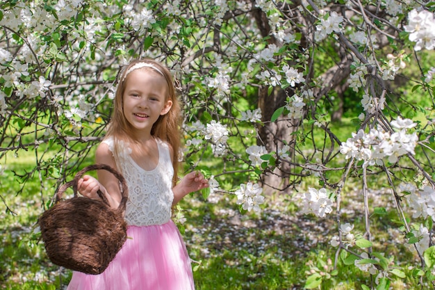 Adorável menina com cesto de palha no pomar de florescimento