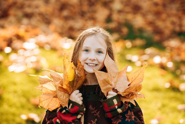 Adorável menina com folhas de outono no parque de beleza Menina feliz rindo e jogando lea