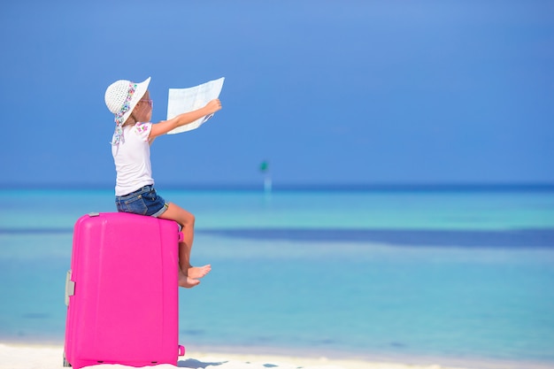 Adorável menina com grande bagagem e mapa da ilha na praia branca