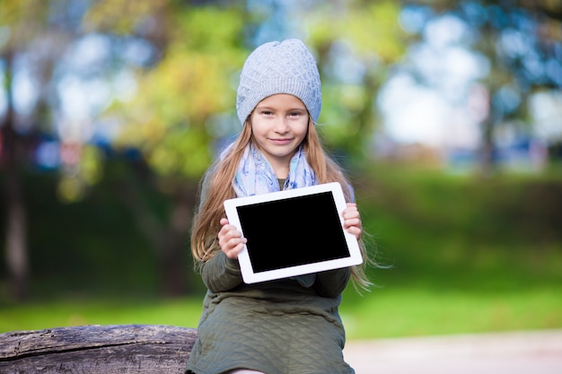 Adorável menina com tablet pc ao ar livre em dia ensolarado de outono