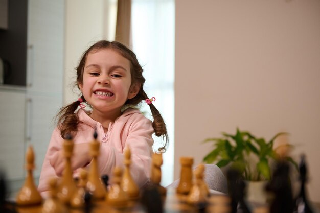 Adorável menina de 4 anos jogando xadrez em casa. jogos de tabuleiro intelectuais inteligentes para crianças, desenvolvimento lógico, conceito de educação