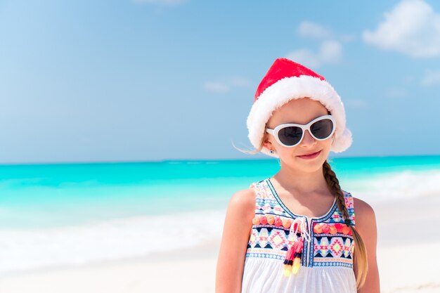 Adorável menina de chapéu de Papai Noel durante as férias de praia de Natal