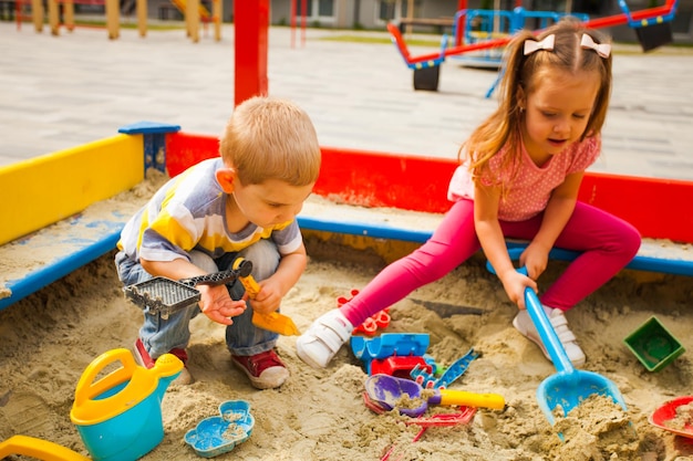 Adorável menina e menino brincando em uma caixa de areia