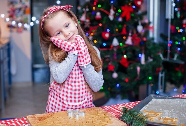 Adorável menina em luvas usava assar biscoitos de gengibre de Natal