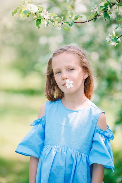 Adorável menina em um jardim de maçãs em flor num lindo dia de primavera