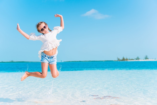 Adorável menina em uma praia tropical de férias, espirrando água rasa