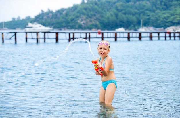 Adorável menina está nadando no mar e brincando com uma pistola de água. turquia