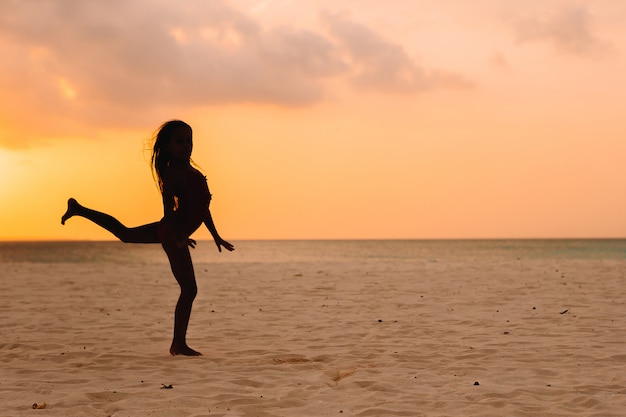 Adorável menina feliz na praia branca ao pôr do sol.