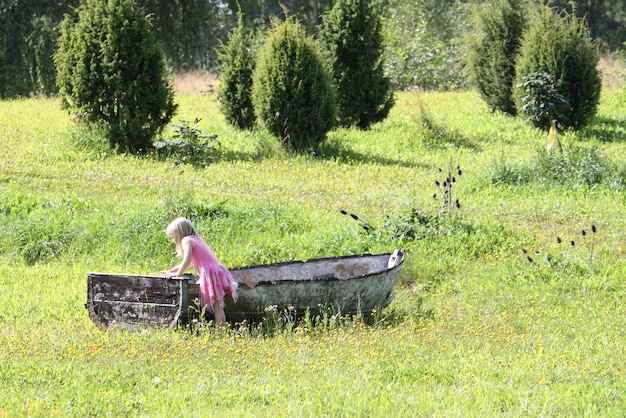 Adorável menina loira brincando em um velho barco de madeira no parque de verão