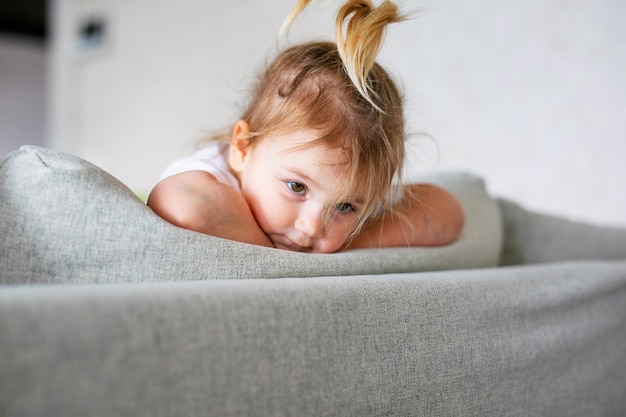 Adorável menina no quarto branco ensolarado. Criança recém-nascida relaxando em uma cama azul. Berçário para crianças pequenas. Criança recém-nascida durante o tempo de barriga com brinquedos em uma janela.