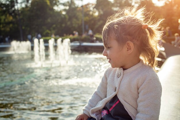 Adorável menina olhando para as fontes do parque em um dia ensolarado