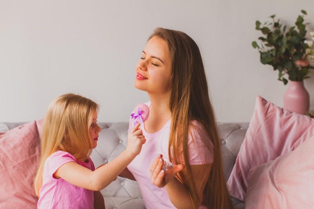 Foto adorável menina segurando o patch rosa aplicando perfume ou creme no pescoço de mathers jovem mulher sentada com os olhos fechados enquanto sua filha aplicando cosméticos em sua pele