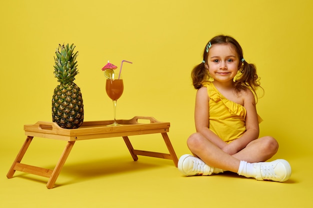 Adorável menina sentada em um fundo amarelo perto de uma bandeja de bambu