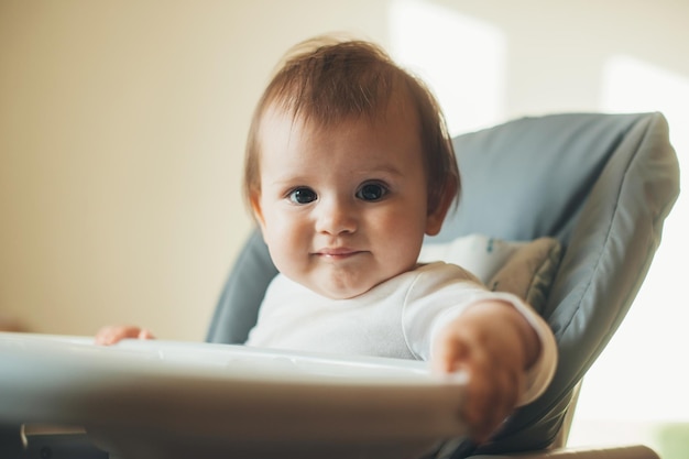 Adorável menina sentada em uma cadeira alta e sorrindo pronta para alimentar os cuidados com o bebê linda menina