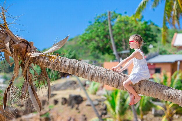 Adorável menina sentada na palmeira durante as férias de verão na praia branca