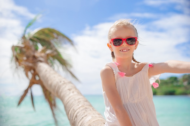Adorável menina sentada na palmeira durante as férias de verão na praia branca