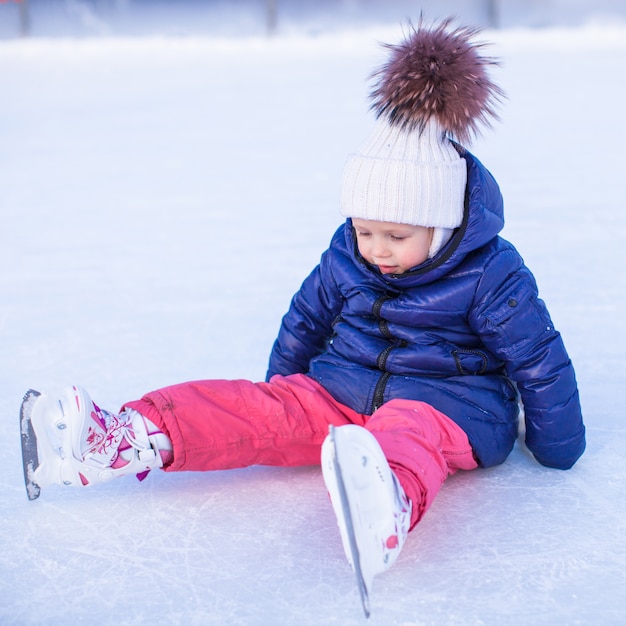 Adorável menina sentada no gelo com patins após a queda