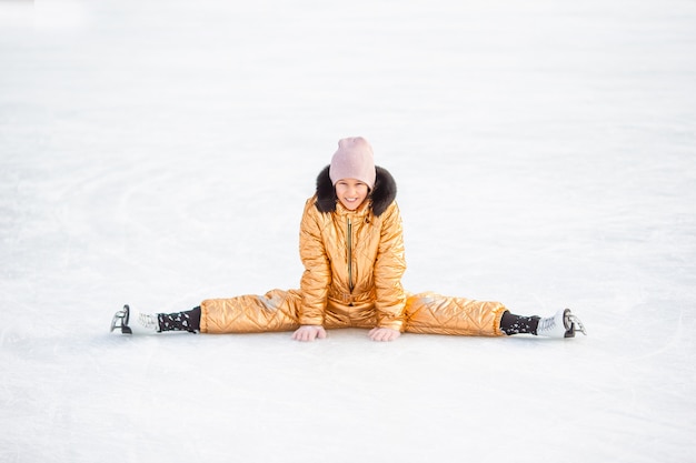 Adorável menina sentada no gelo com patins após o outono