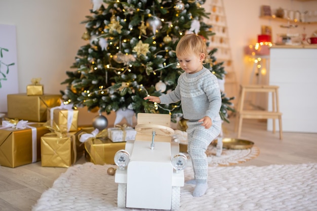 Adorável menina sentada perto da árvore de natal com luzes festivas e presentes de natal, natal e ano novo