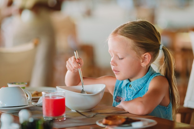 Adorável menina tomando café da manhã no café ao ar livre